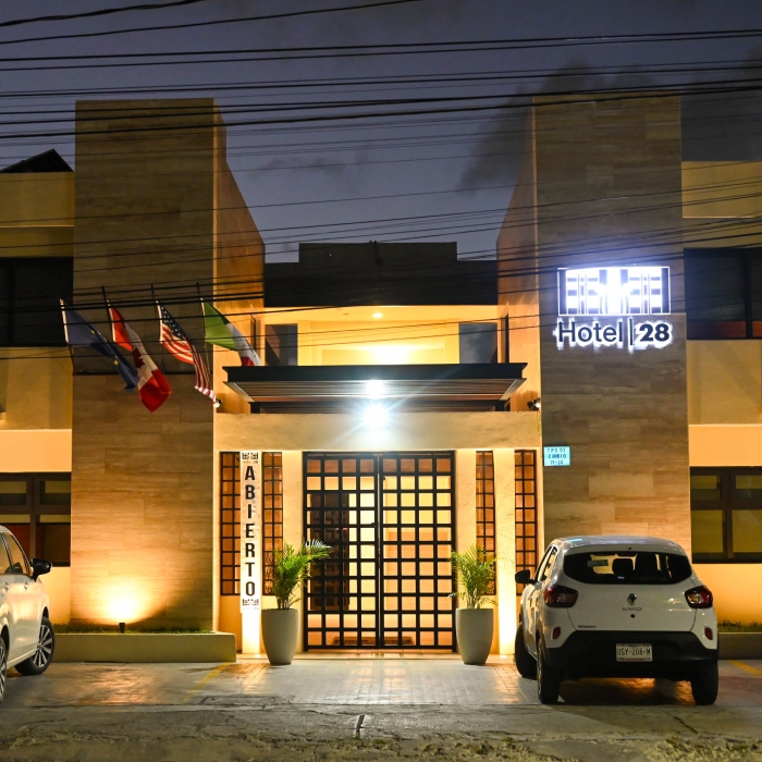 Entrada iluminada de un hotel moderno con autos estacionados al frente.