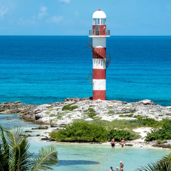 Faro rayado rojo y blanco en isla rocosa, personas nadando en el mar turquesa.