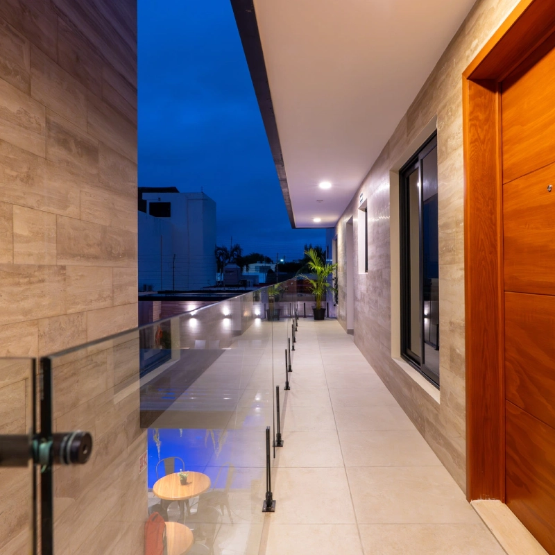 Pasillo moderno con paredes de madera y barandilla de vidrio, al anochecer.