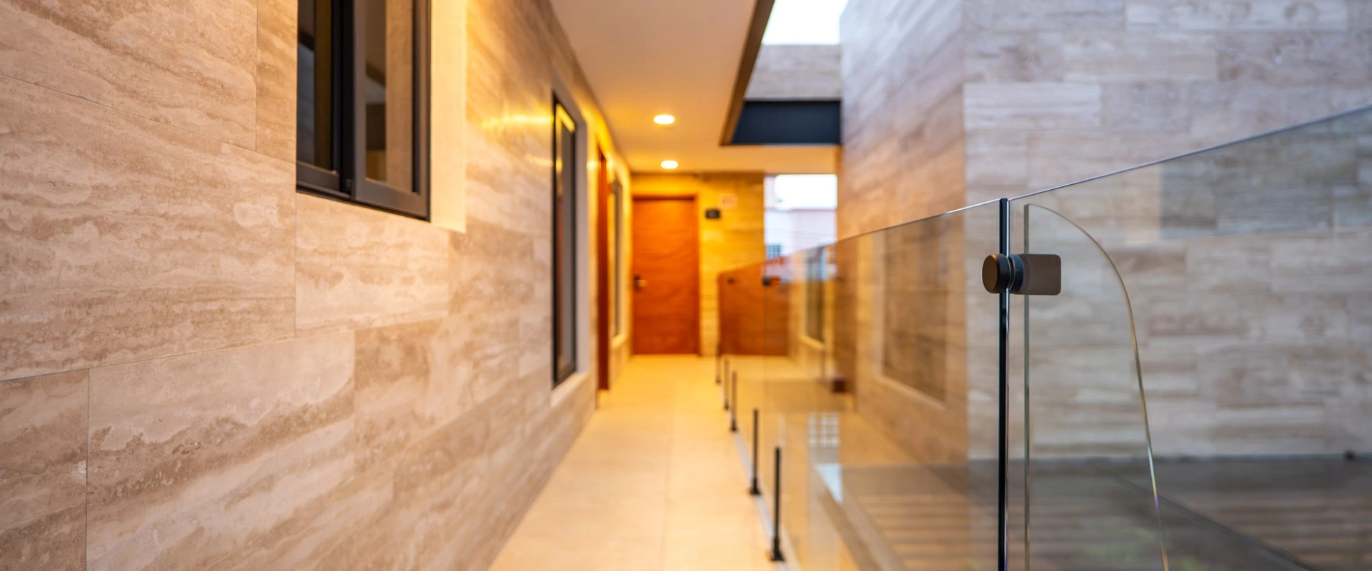 Pasillo moderno con pared de m&aacute;rmol y barandilla de cristal.