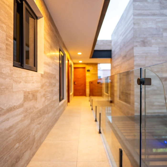 Pasillo moderno iluminado con baranda de vidrio y paredes de piedra clara.