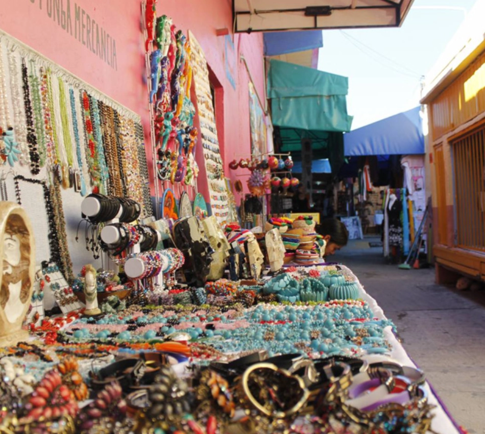 Mercado callejero con puestos de joyer&iacute;a colorida y un pasillo al fondo.