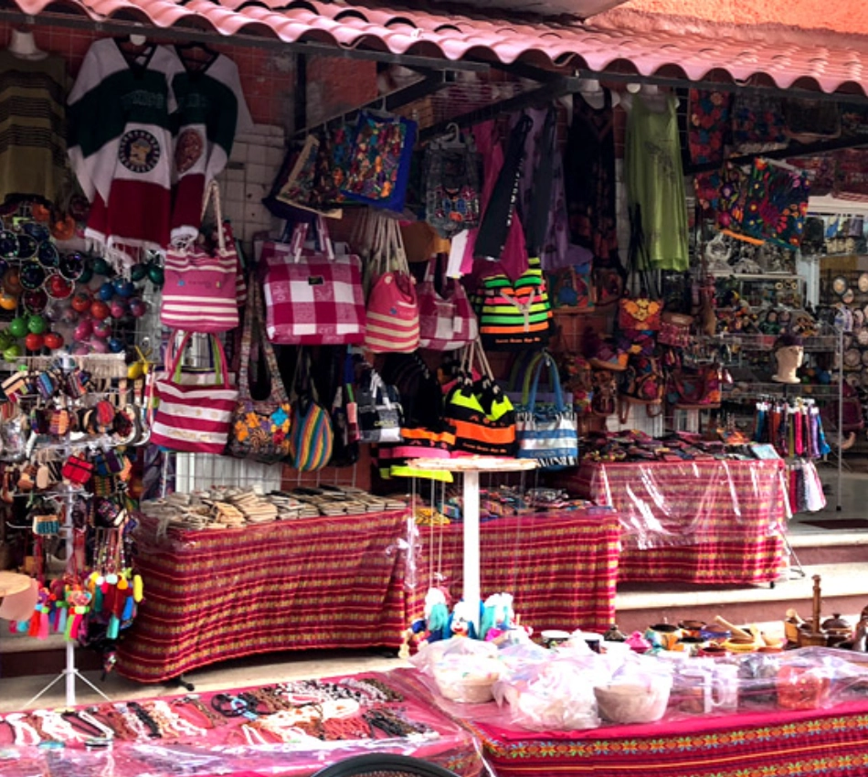 Puesto colorido de mercado con artesan&iacute;as y ropa colgadas y en mesas.