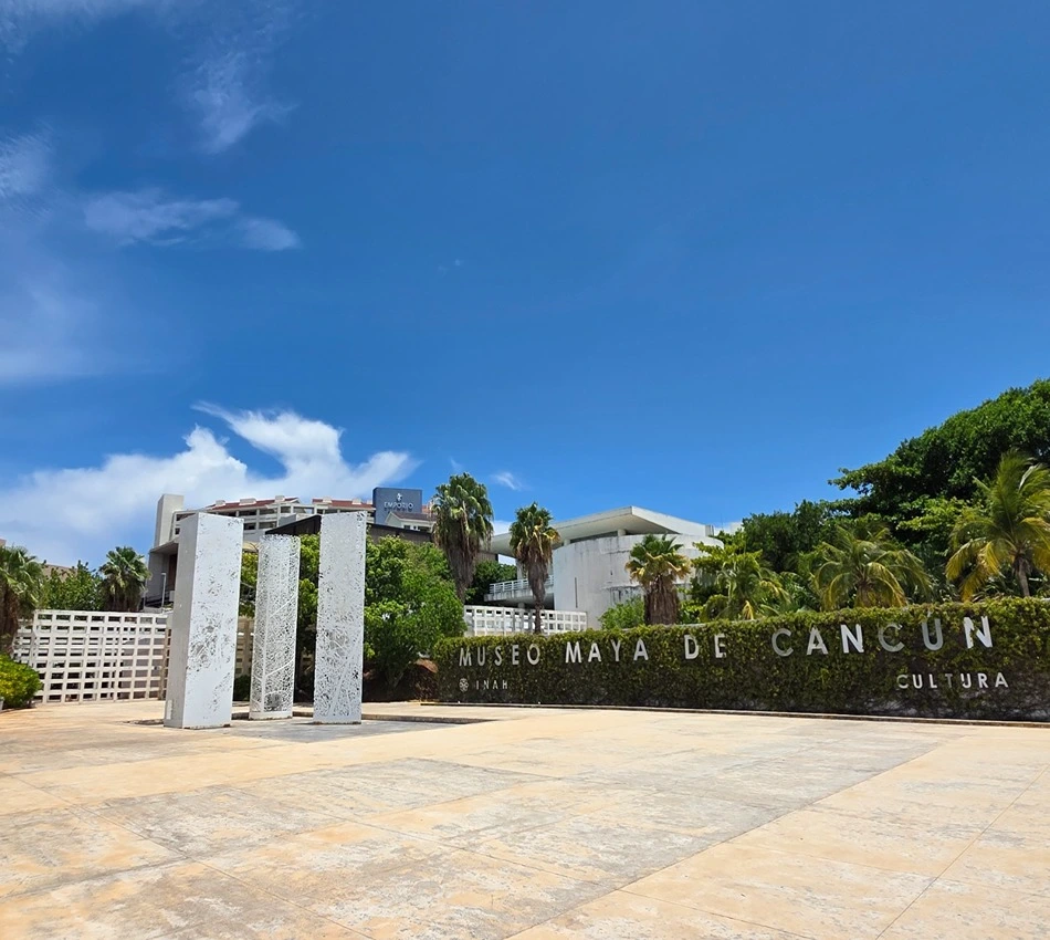 Entrada del Museo Maya de Canc&uacute;n con cielo despejado y palmeras.
