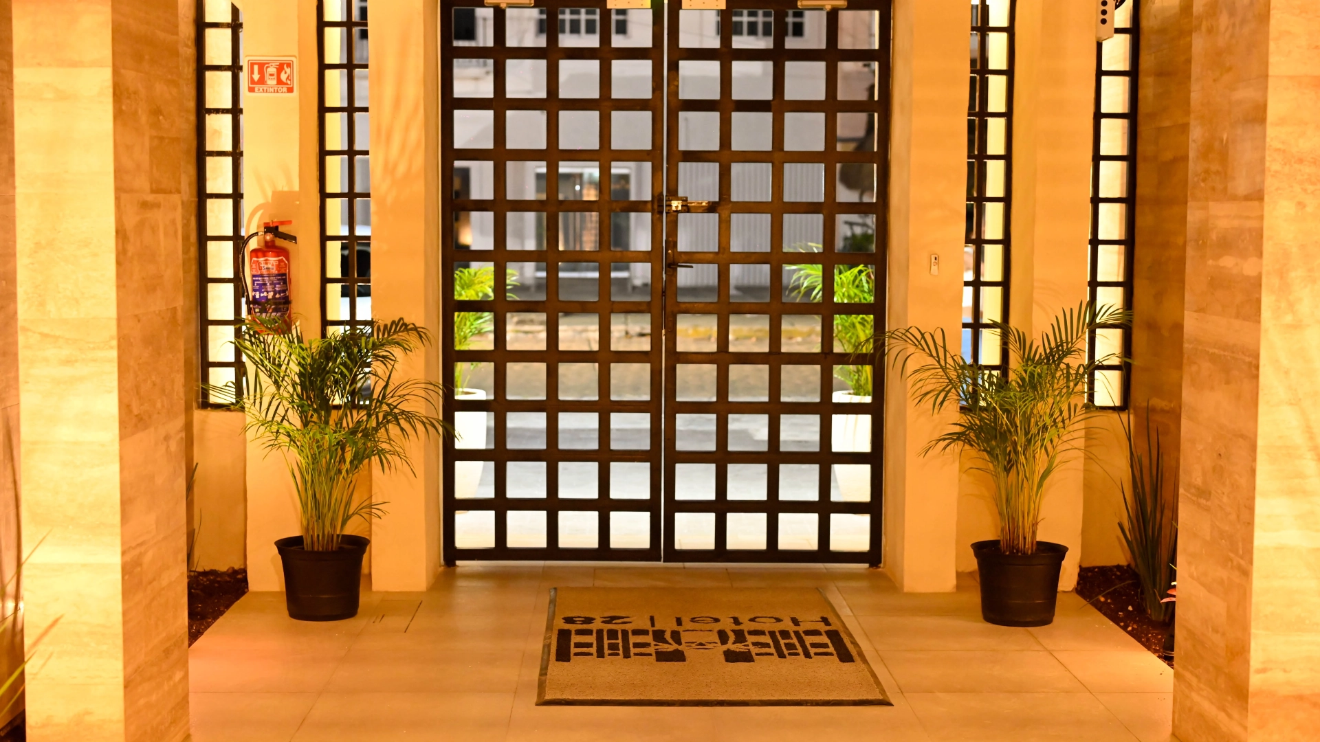 Puerta de rejilla con macetas y extintor en pasillo iluminado.