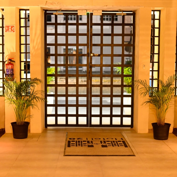 Puerta de entrada con rejas negras, alfombra y plantas a los lados.
