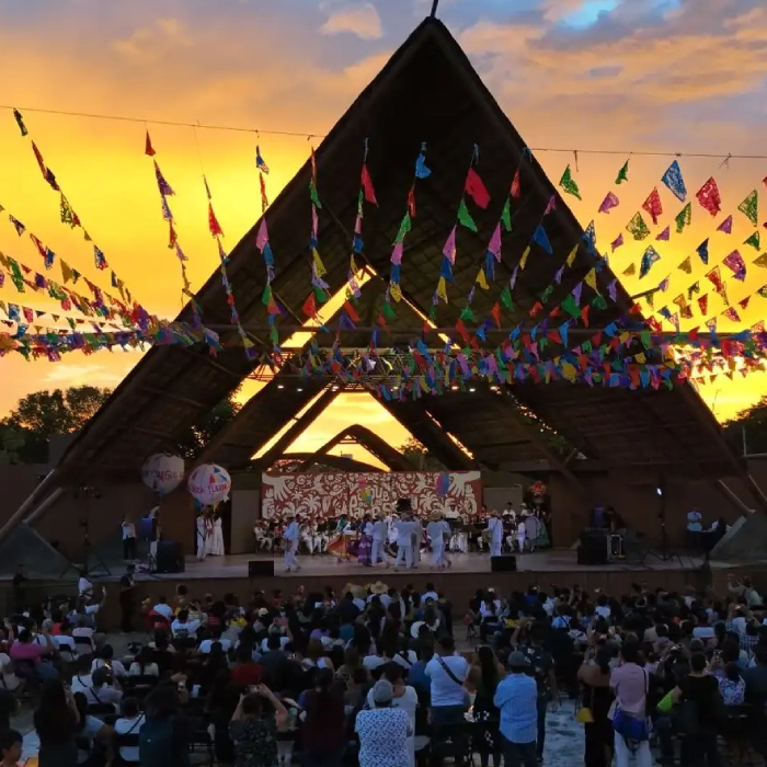 Escenario iluminado al atardecer, con p&uacute;blico y coloridas banderillas colgantes.