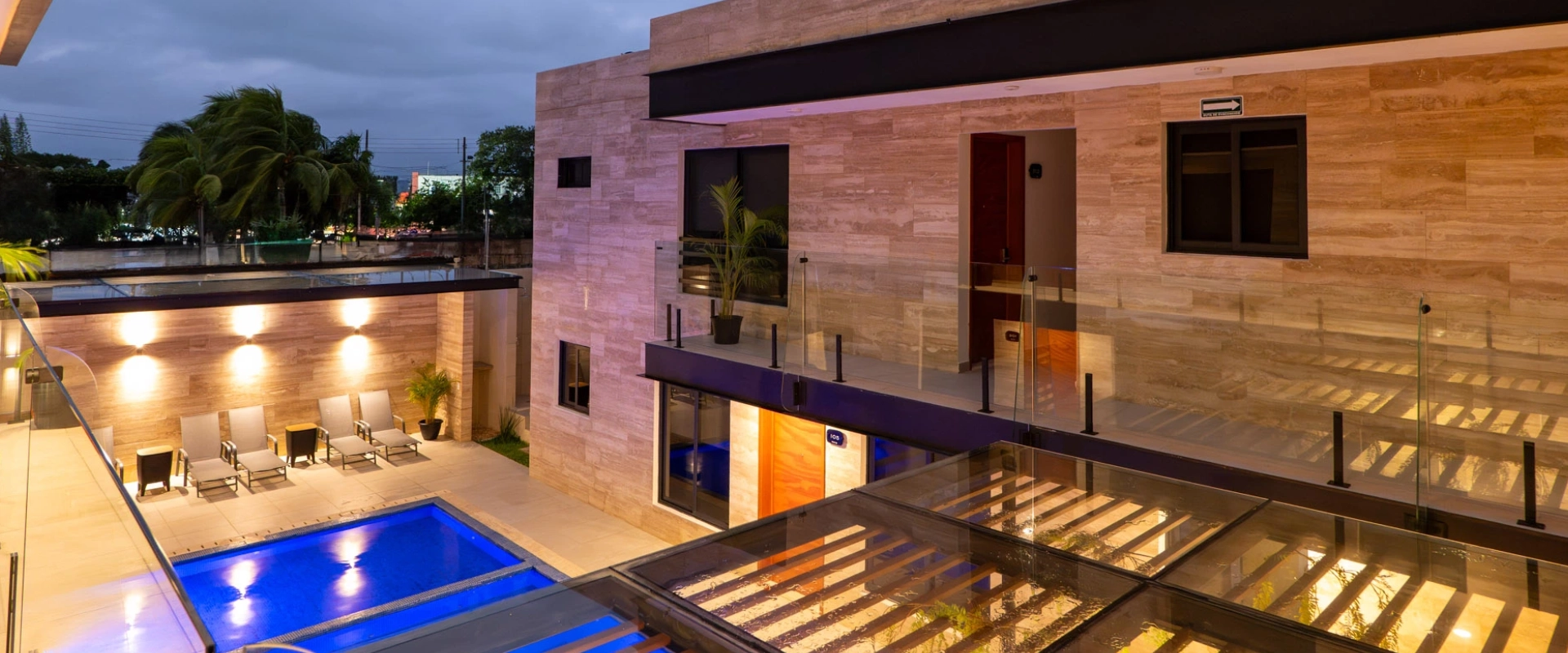 Moderno edificio con piscina iluminada y terrazas al anochecer.