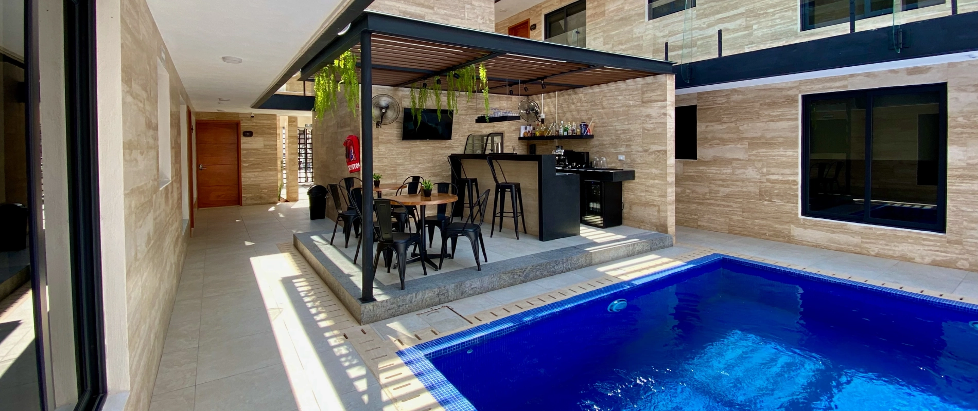 Piscina con bar y mesas en un patio moderno y soleado.