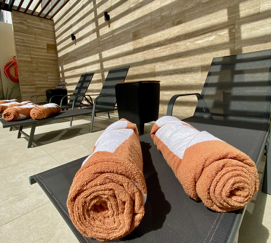 Toallas enrolladas en tumbonas junto a una pared de piedra.