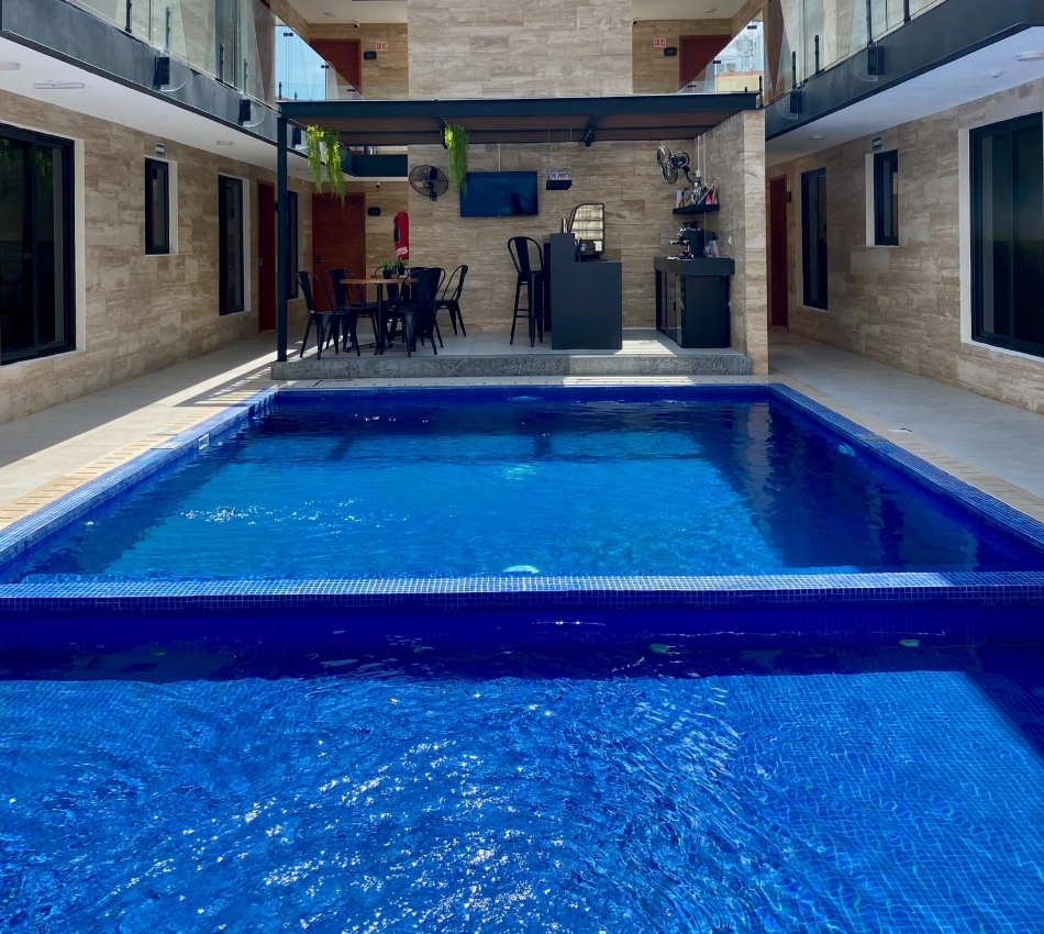 Piscina en un hotel con sillas y mesa cerca del bar bajo un techo cubierto.