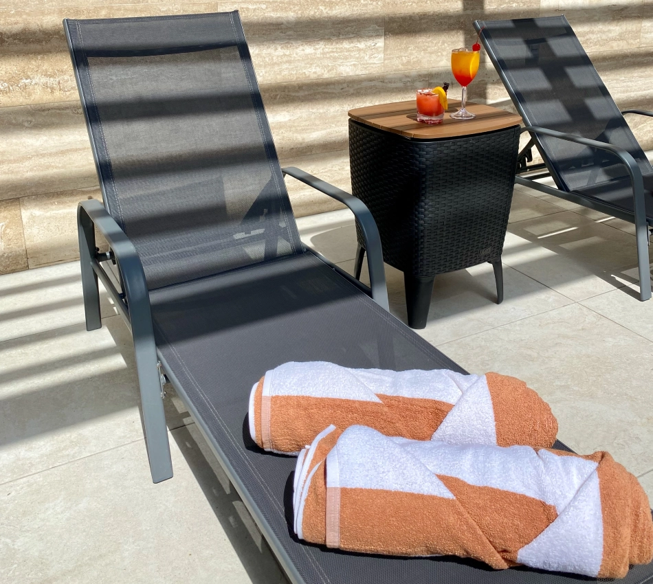 Tumbonas con bebidas y toallas junto a una mesa en una terraza soleada.