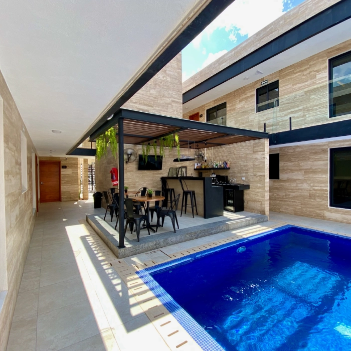 Piscina junto a una terraza con bar y sillas, rodeada de paredes beige.