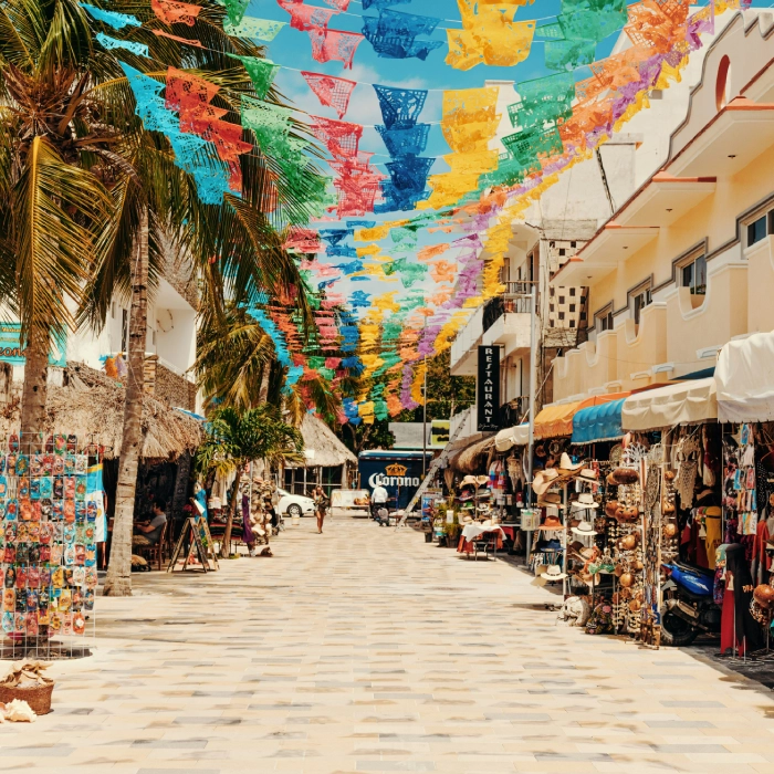 Calle con banderines de colores, tiendas y palmeras a los lados.