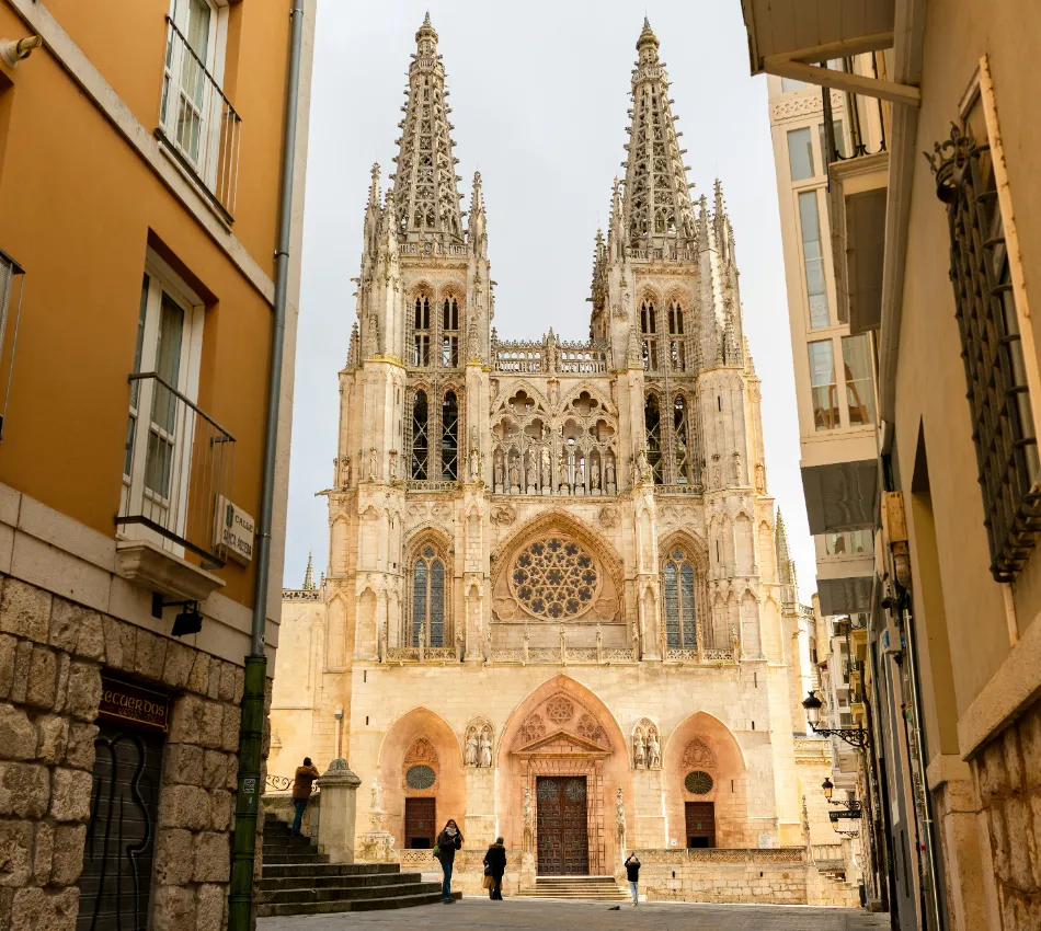 Catedral g&oacute;tica con altas torres, vista desde una calle estrecha entre edificios.