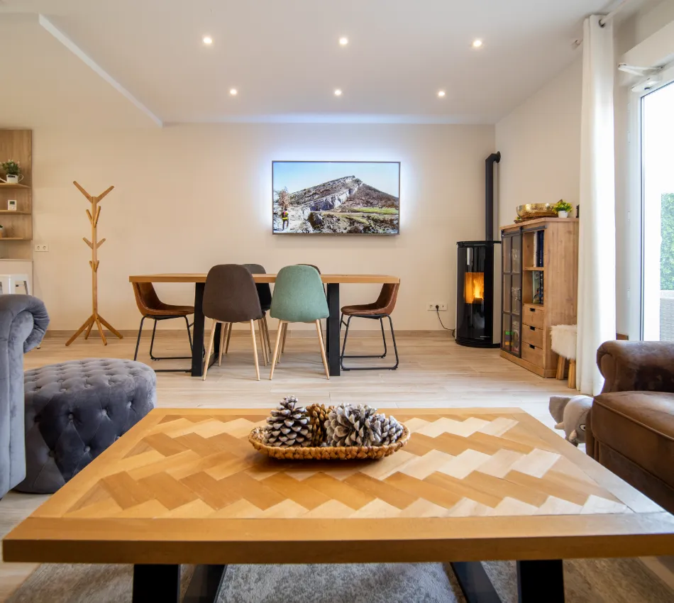 Sala moderna con mesa de centro, sillas coloridas y chimenea; TV en la pared.