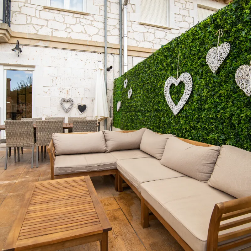 Sala exterior con sof&aacute; beige, mesa de madera y pared verde con adornos de corazones.