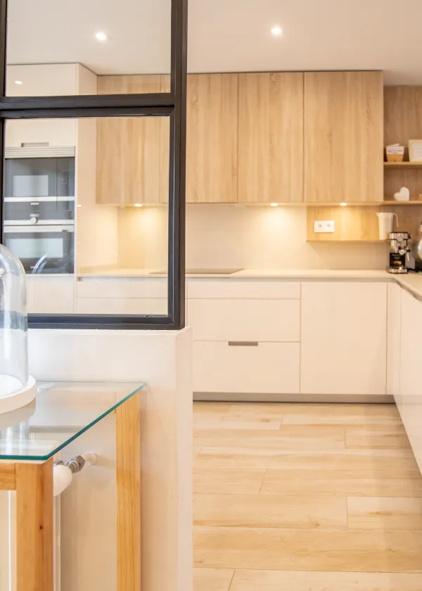 Cocina moderna con muebles de madera clara, encimeras blancas y luz suave.