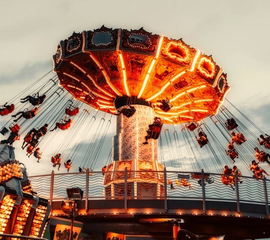 Atracci&oacute;n giratoria iluminada al anochecer con personas disfrutando del paseo.