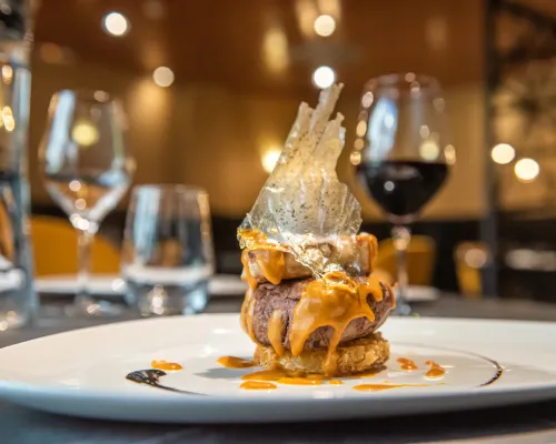 Hamburguesa gourmet con salsa y copas de vino en el fondo borroso.