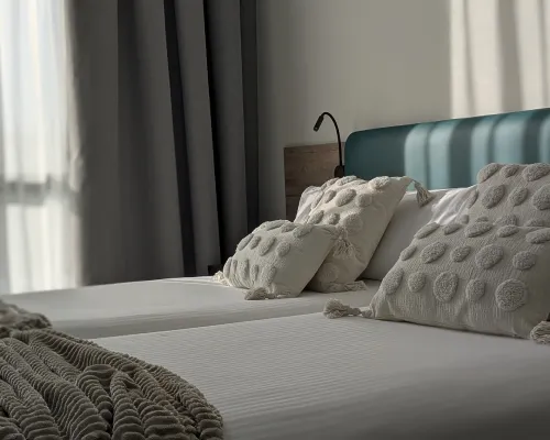 Cama con almohadas decorativas y luz natural entrando por la ventana.