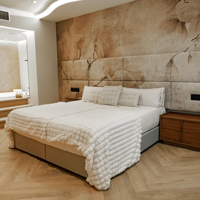 Cama con mantas blancas en habitaci&oacute;n moderna con pared decorada y luz tenue.