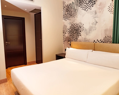 Habitaci&oacute;n de hotel con cama doble y decoraci&oacute;n de pared abstracta en tonos oscuros.