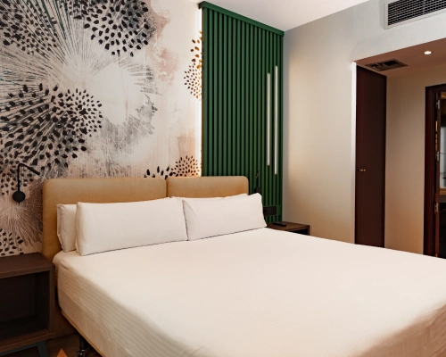 Habitaci&oacute;n moderna con cama doble, mural art&iacute;stico y pared verde.