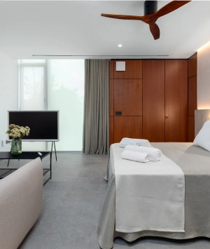 Habitaci&oacute;n moderna con cama, TV, armario y ventilador en el techo.