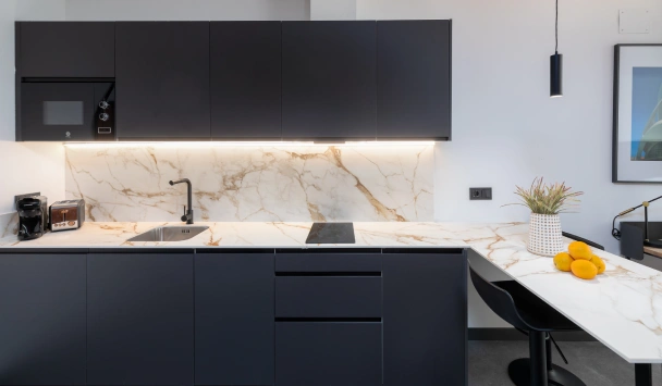 Cocina moderna con encimera de m&aacute;rmol y gabinetes oscuros.