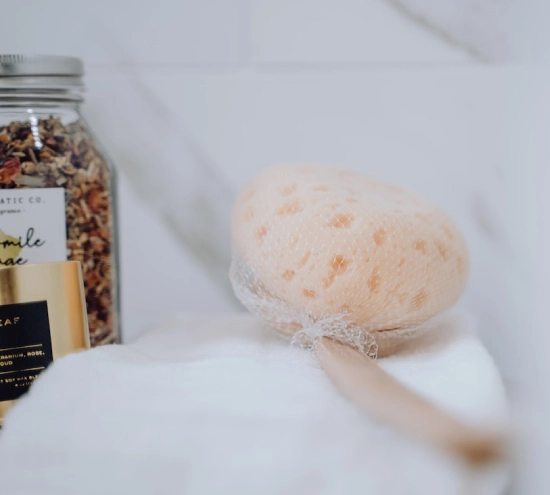 Esponja de ba&ntilde;o y frasco de hierbas sobre una toalla blanca.