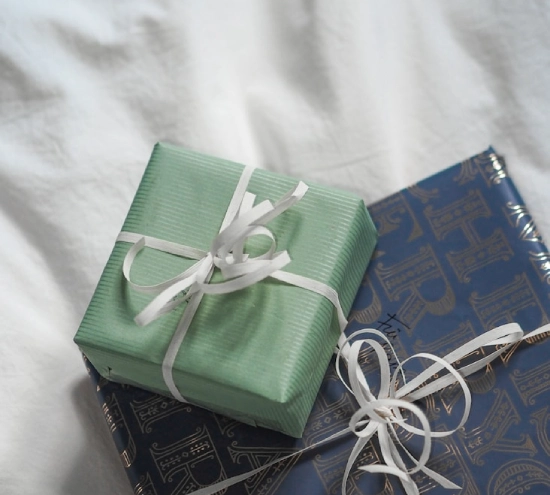 Regalos envueltos con lazos blancos sobre una tela blanca.