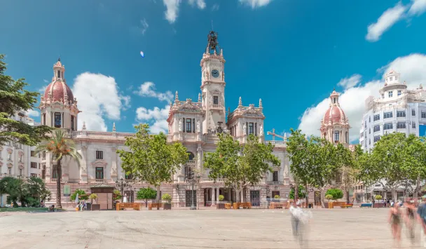 Plaza y edificio hist&oacute;rico con cielo azul y &aacute;rboles.