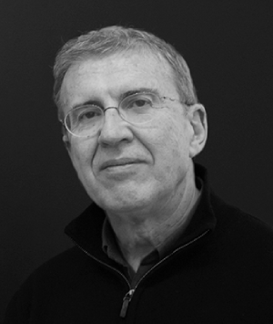 No s&eacute; qui&eacute;n es la persona en la imagen. Hombre con gafas, su&eacute;ter oscuro sobre fondo gris.