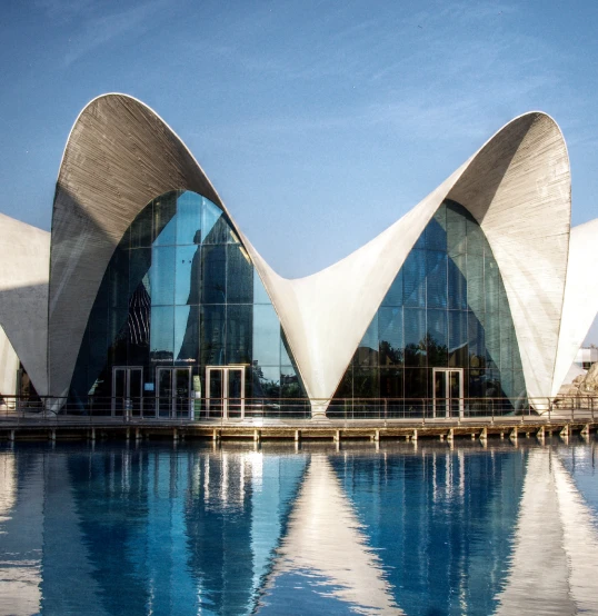Edificio moderno con techo curvo reflejado en agua.