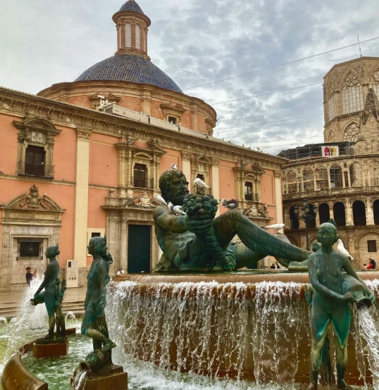 Fuente con figuras y edificio hist&oacute;rico de fondo.