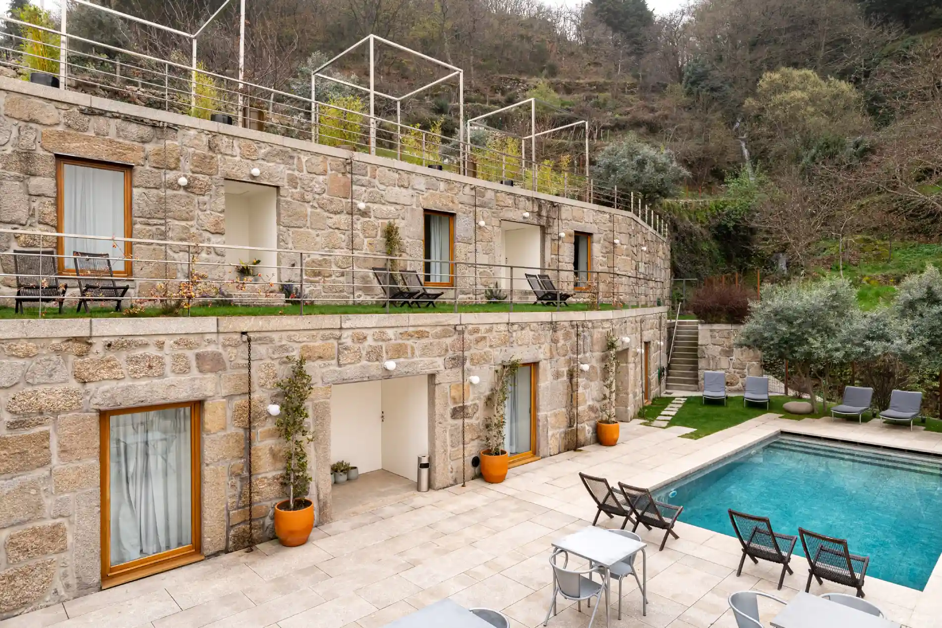 Casa de pedra com dois andares, terra&ccedil;o verde e piscina ao lado da montanha.