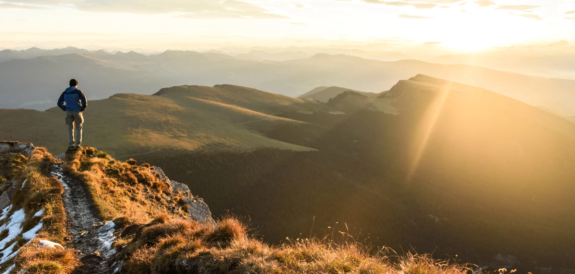 Pessoa contemplando o nascer do sol em uma paisagem montanhosa.