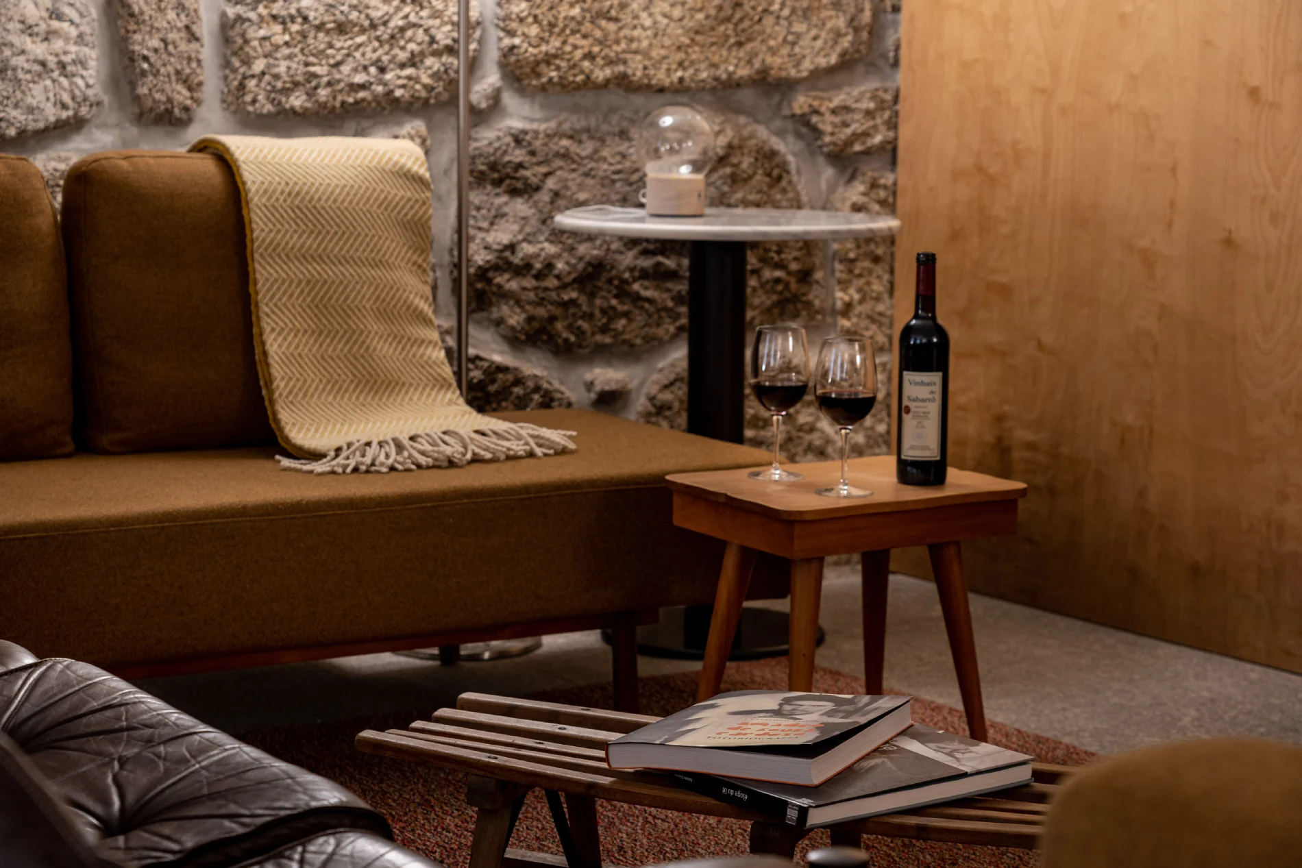Sala aconchegante com sof&aacute;, manta, vinho e livros em uma mesa de centro.