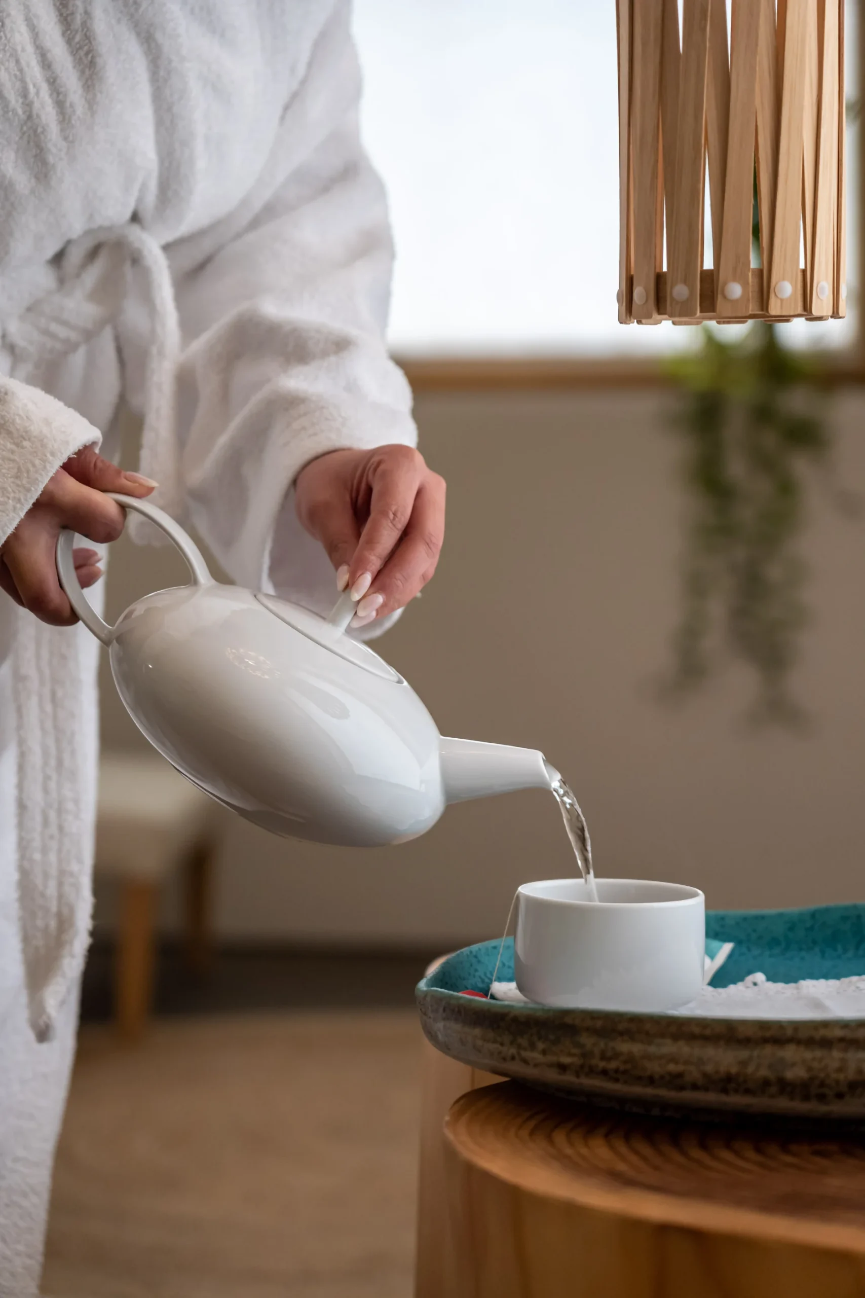 Pessoa servindo ch&aacute; em uma x&iacute;cara branca sobre bandeja, usando um roup&atilde;o branco.