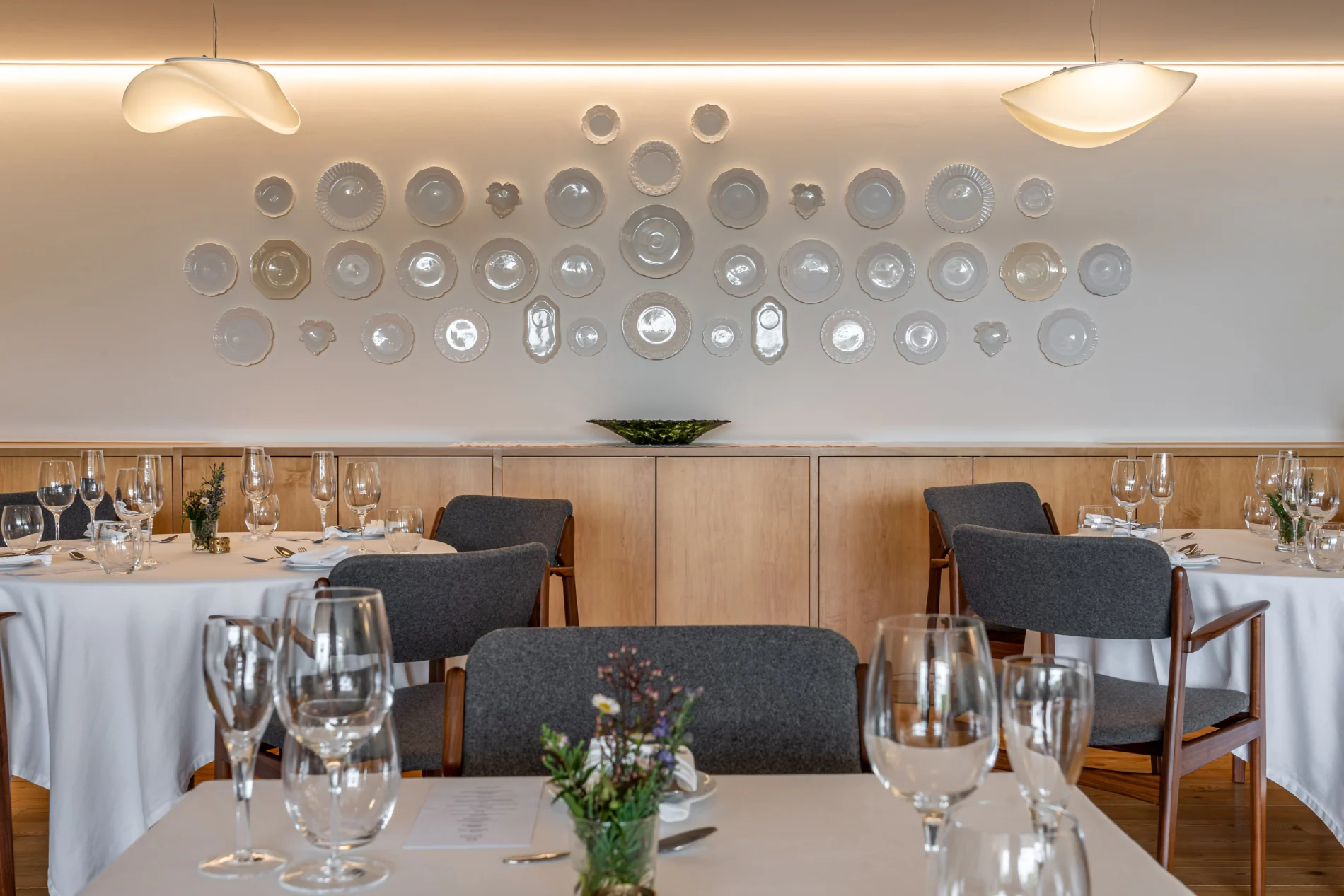 Restaurante elegante com mesas postas e paredes decoradas com pratos brancos.