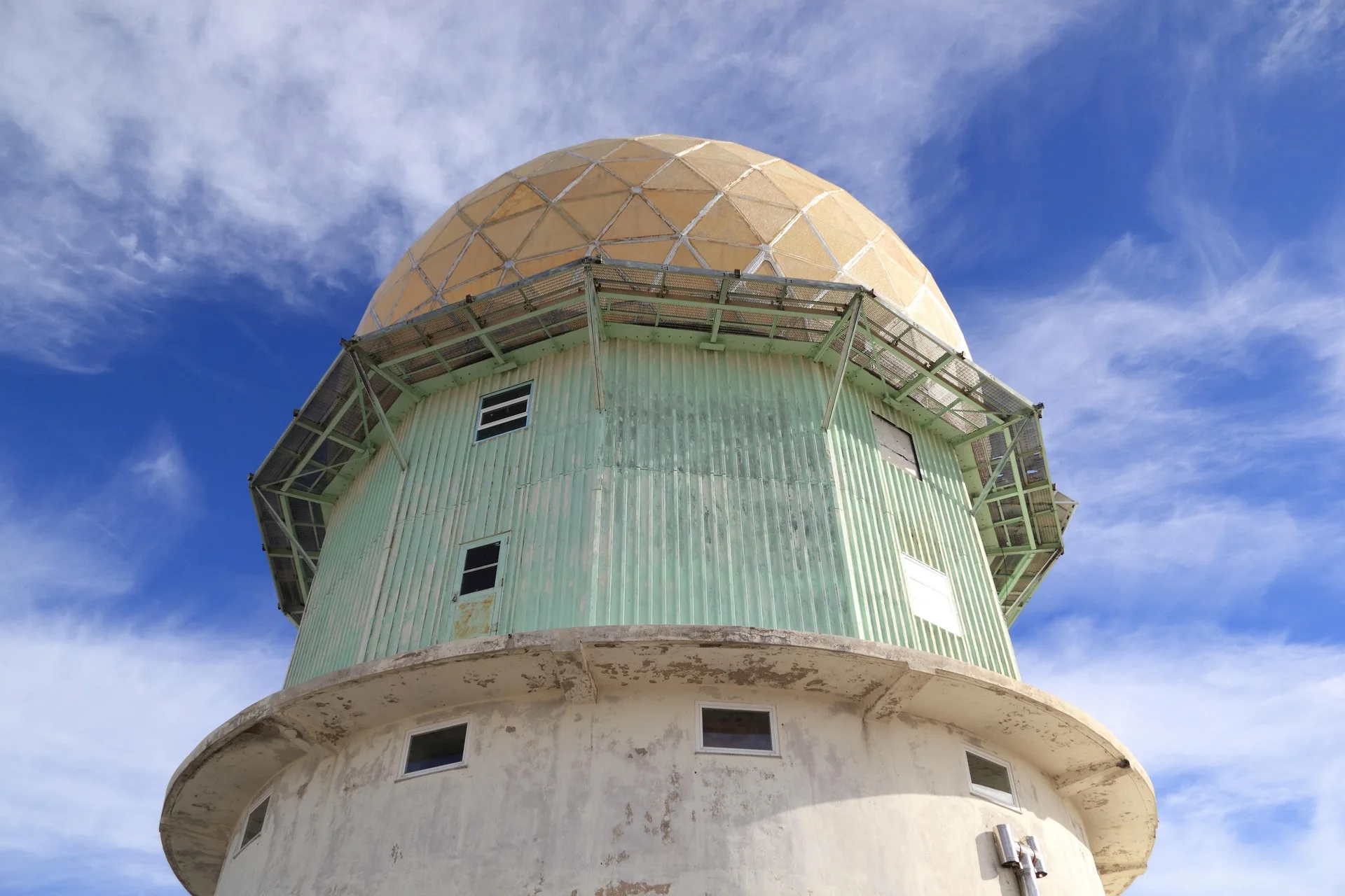 C&uacute;pula de radar em estrutura verde contra c&eacute;u azul e nuvens brancas.