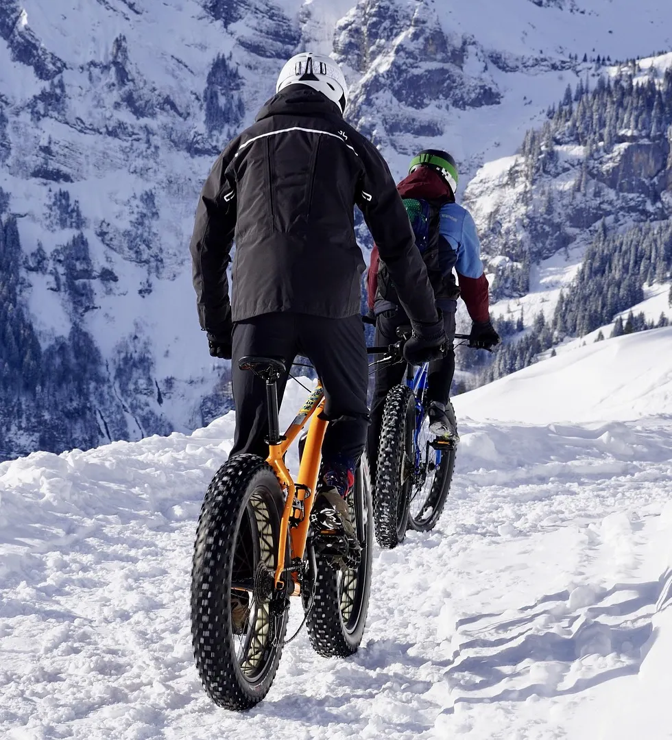 Ciclistas pedalando em uma trilha de neve nas montanhas, equipados com bicicletas de pneus largos.