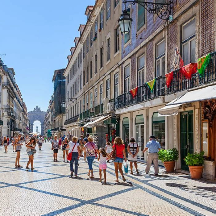 Rua movimentada com pedestres e arco ao fundo em dia ensolarado.