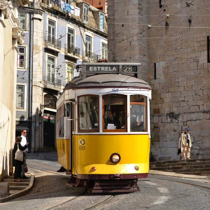 El&eacute;trico amarelo na rua de Lisboa, com pr&eacute;dios e pessoas ao fundo.