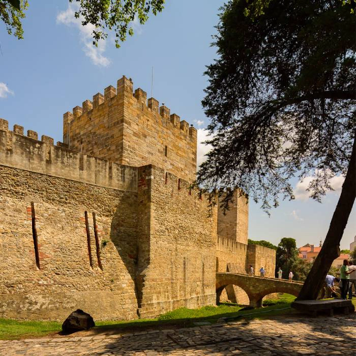 Castelo medieval com ponte de pedra e torres sob c&eacute;u azul claro.