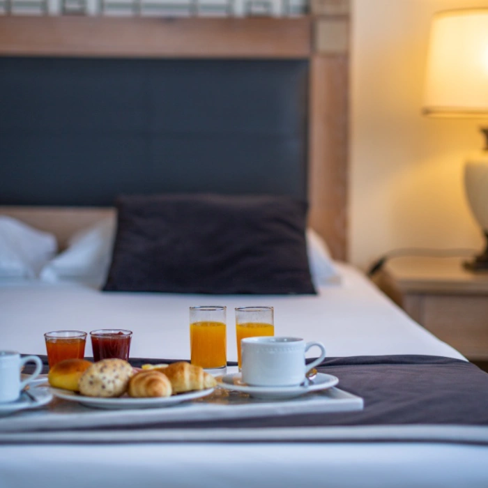 Caf&eacute; da manh&atilde; na cama com sucos, caf&eacute; e p&atilde;es numa bandeja.