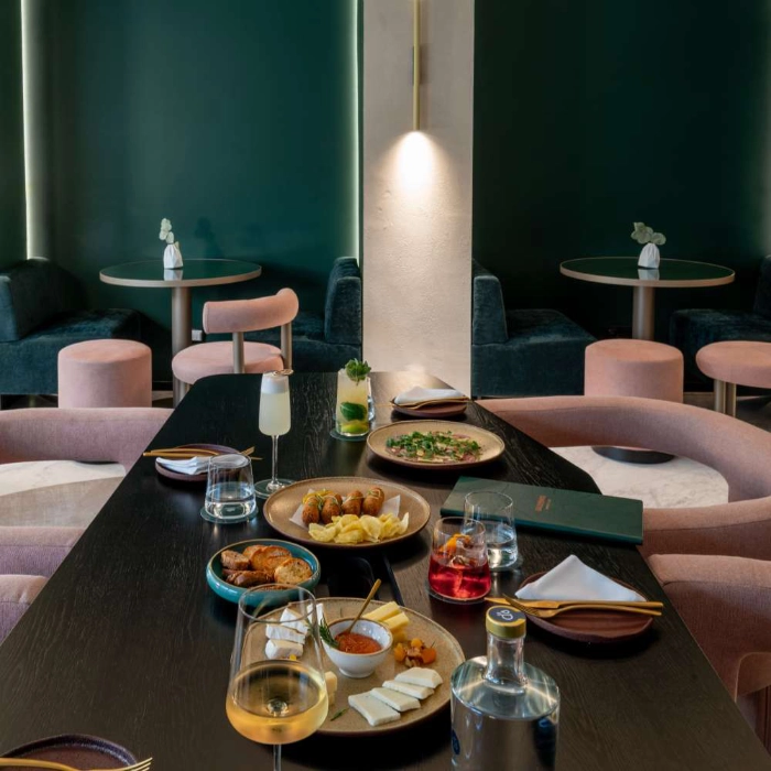Mesa de restaurante com pratos e bebidas, cadeiras rosa, sala iluminada.