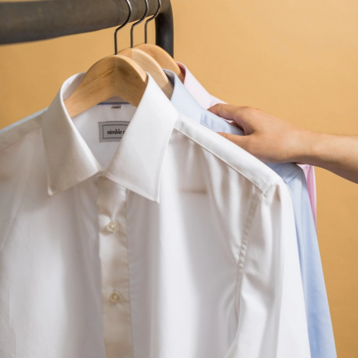 Camisas em cabides, m&atilde;o escolhe uma em fundo bege.