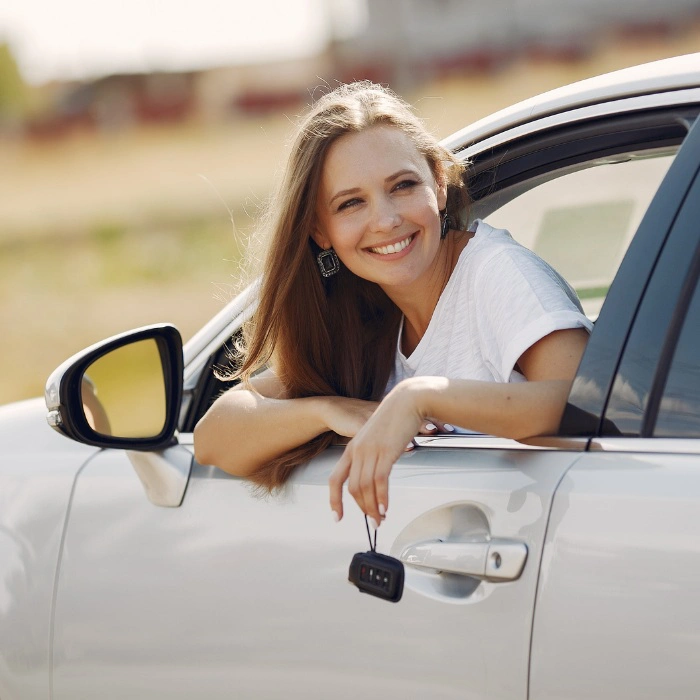 Mulher sorrindo apoiada na janela de um carro branco.